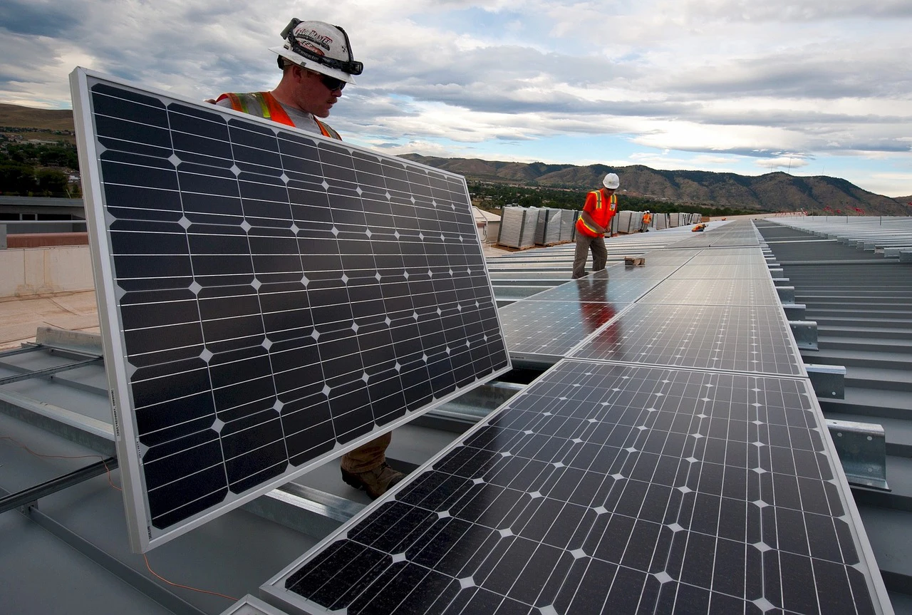 Workers installing rows of solar panels on a metal roof