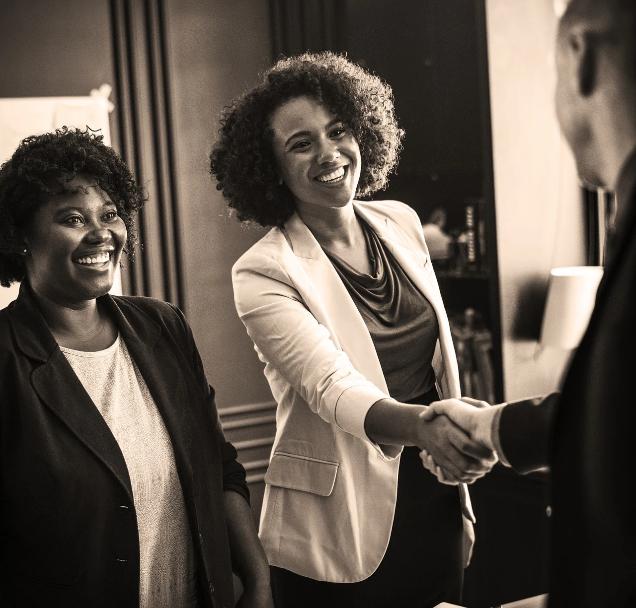 Two smiling women shaking hands with a businessman in a sepia-toned office