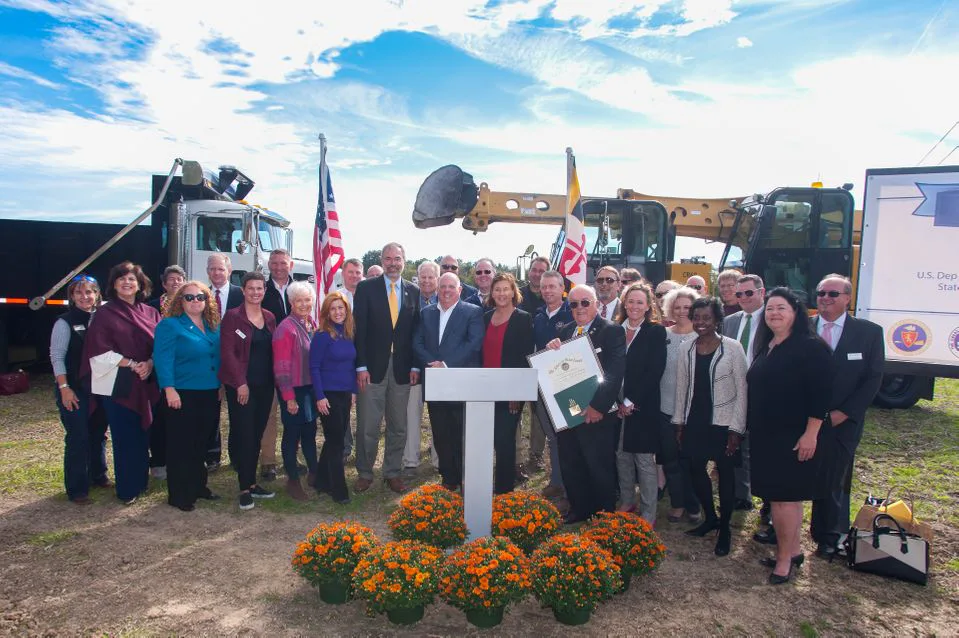 Officials gathered at a groundbreaking ceremony with a podium and construction equipment