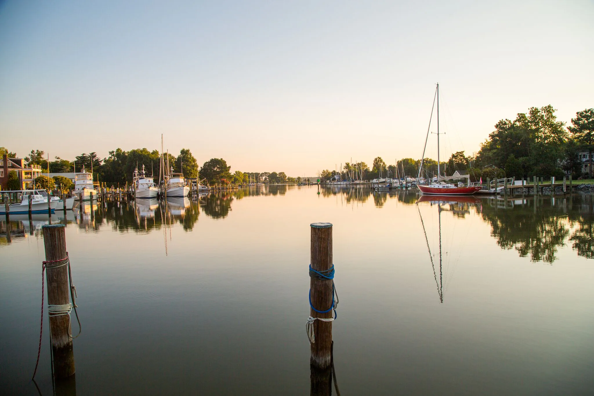 Calm evening view of boats moored at a small harbor with pilings in the water