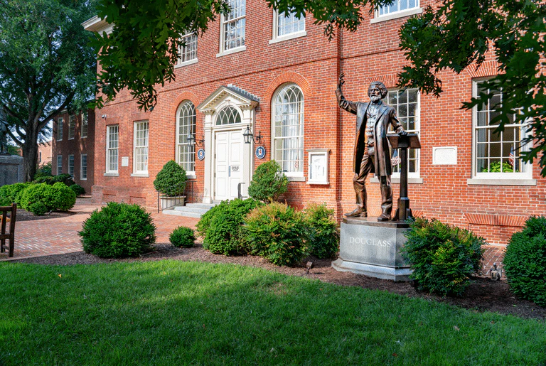 Bronze statue of Frederick Douglass in front of a red brick building