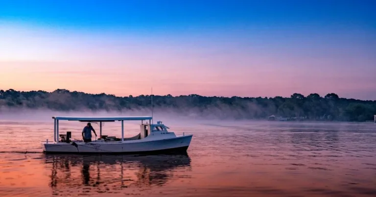 Small open boat with two people on calm water at sunset
