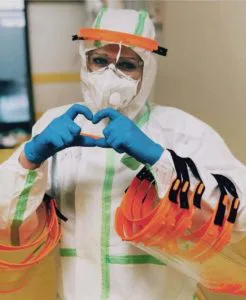 Health worker in protective gear and face shield making a heart with gloved hands