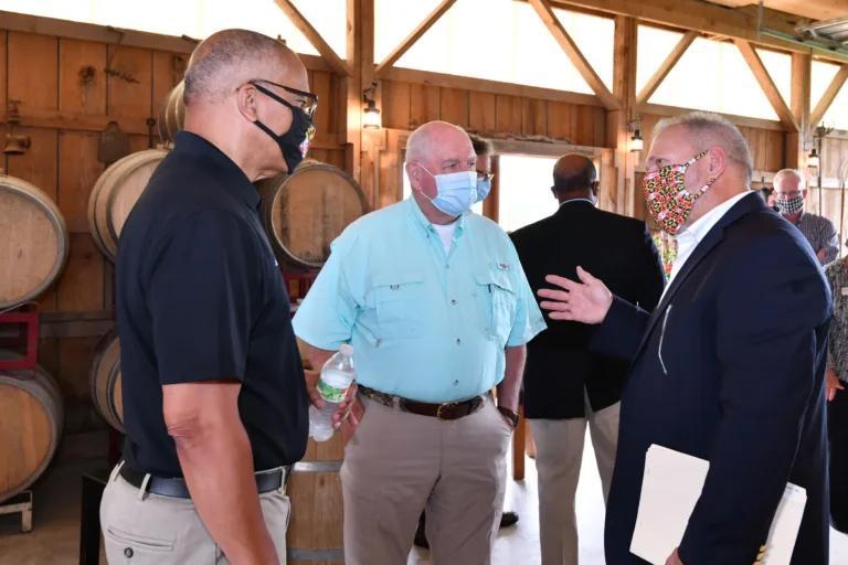 Masked men in conversation among wine barrels in a barrel-lined cellar