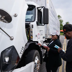 Two people with clipboards inspecting the cab of a white semi truck