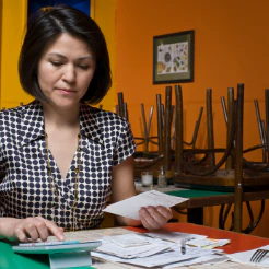 Woman reviewing paperwork at a table in a room with chairs stacked behind her