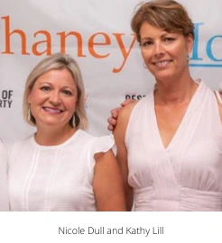 Nicole Dull and Kathy Lill smiling in front of an event banner