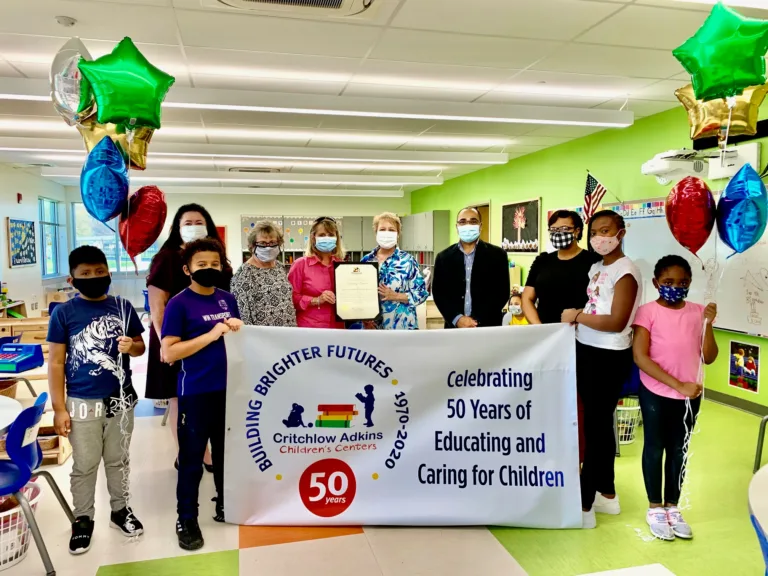 Group holding a Building Brighter Futures banner celebrating 50 years of educating and caring for children