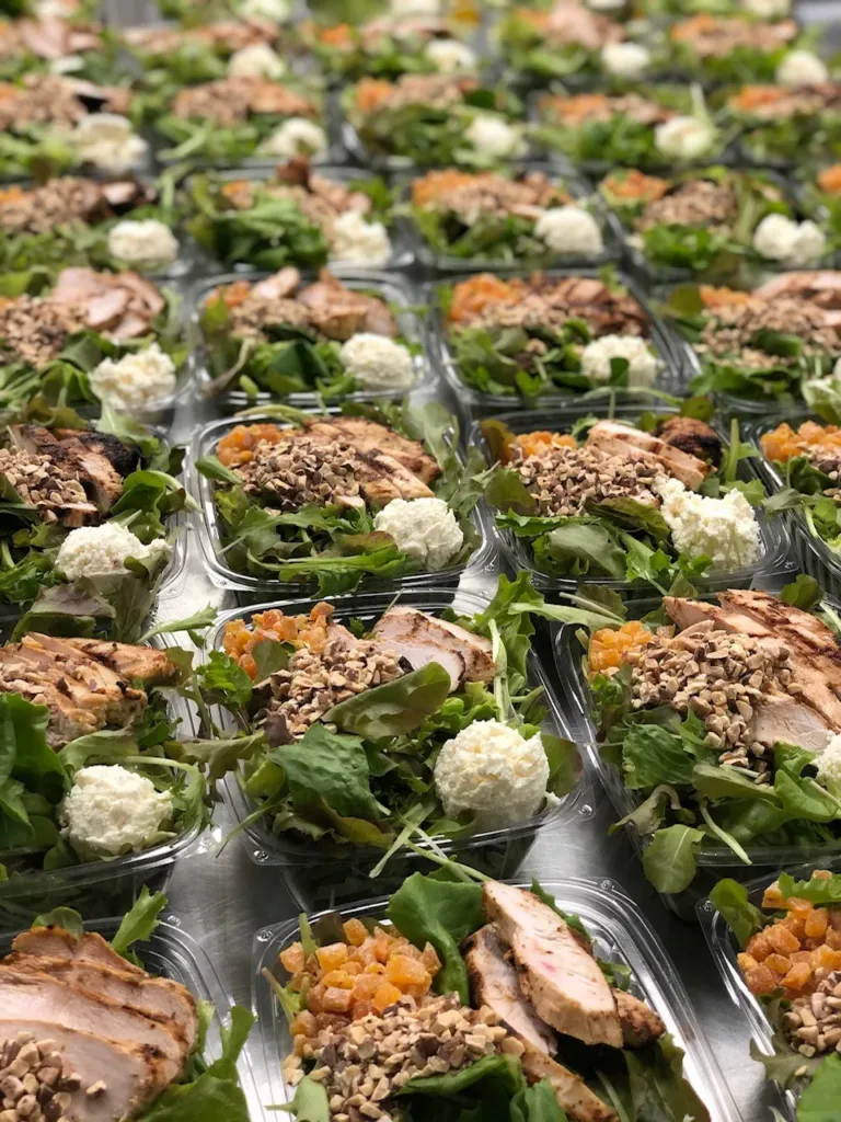 Rows of prepared salad meals with chicken, greens and fruit in plastic containers