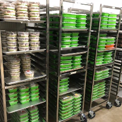 Metal racks holding rows of green-lidded meal containers in a commercial kitchen