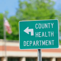 Green road sign reading County Health Department with a left arrow