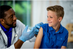 Doctor in blue gloves giving a smiling boy a vaccination in a clinic