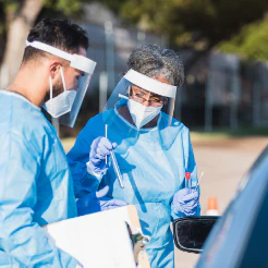 Health workers in face shields and gowns preparing testing swabs at a roadside site