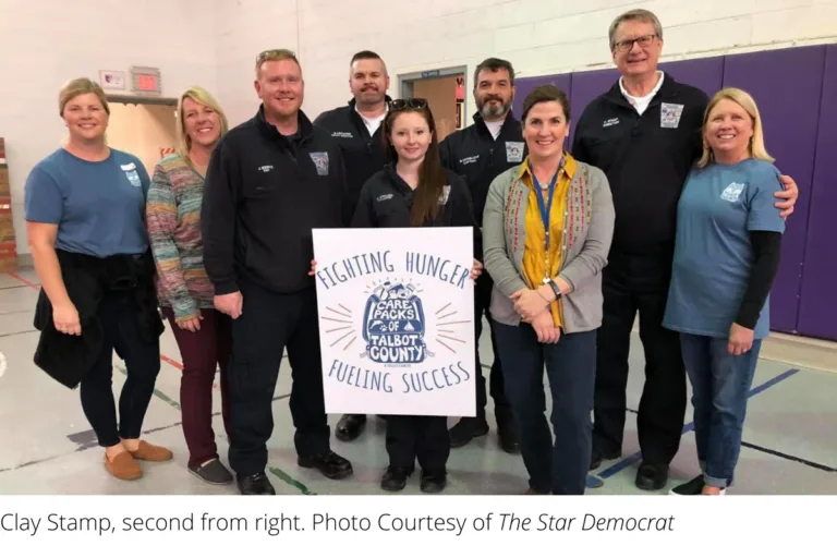 Group holding a Fighting Hunger Feeding Success sign, with Clay Stamp second from right