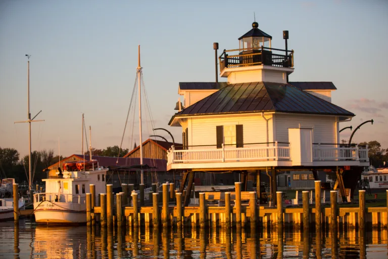 White lighthouse on pilings at dusk beside docked boats