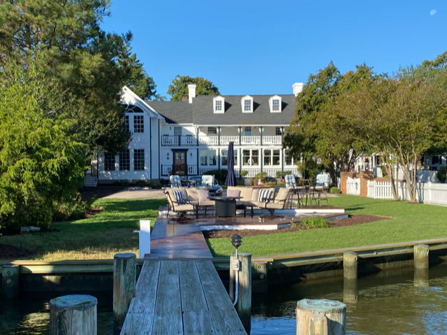 Waterfront white house with dormers, lawn, outdoor seating and a wooden dock