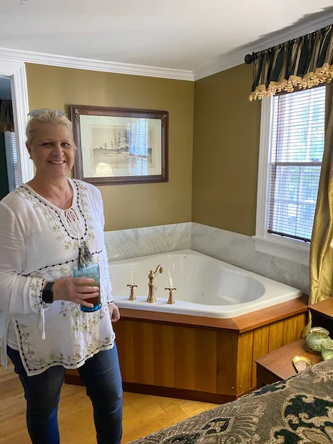 Smiling woman standing beside a corner soaking tub in a room with gold walls