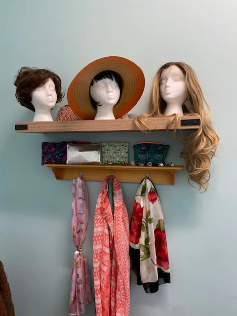 Shelf display of wigs on mannequin heads, a straw hat and hanging scarves