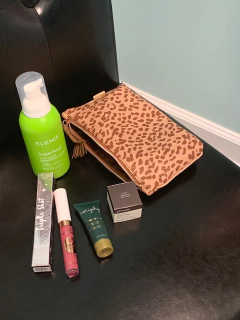 Makeup and skincare products with a leopard-print pouch on a dark chair