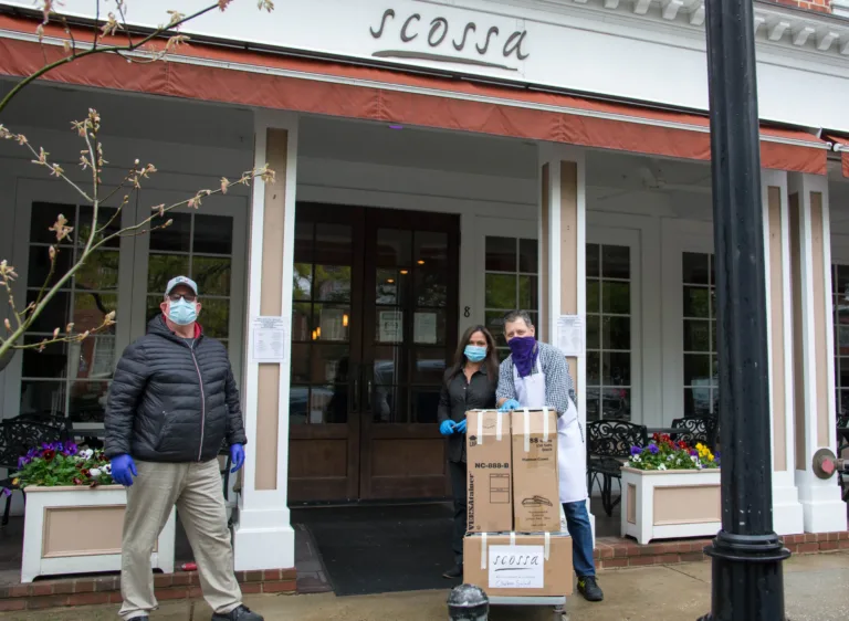 Masked volunteers holding food boxes outside the scossa storefront