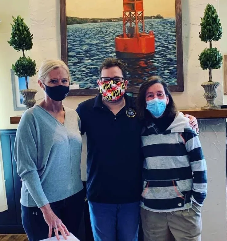 Three masked people posing in front of a painting of a red buoy