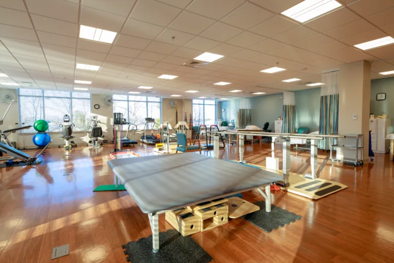 Bright rehabilitation gym with treatment tables and exercise equipment on wood floors