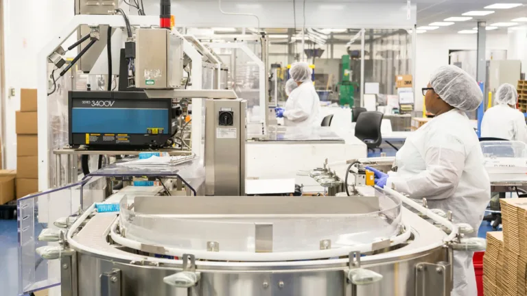 Workers in white cleanroom suits operating a pharmaceutical production line