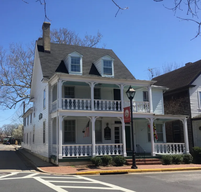White two-story building with a wraparound porch and gray roof