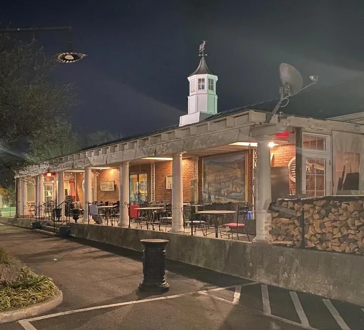 Night view of an open-air restaurant patio with a cupola and firewood stacked on the side