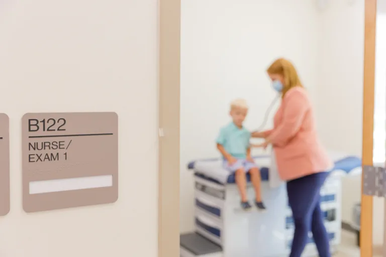 Exam room door labeled B122 Nurse/Exam 1 with a nurse and child inside