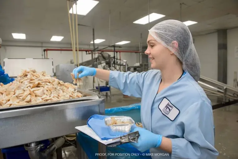 Worker in hairnet and blue smock inspecting seafood on a processing line