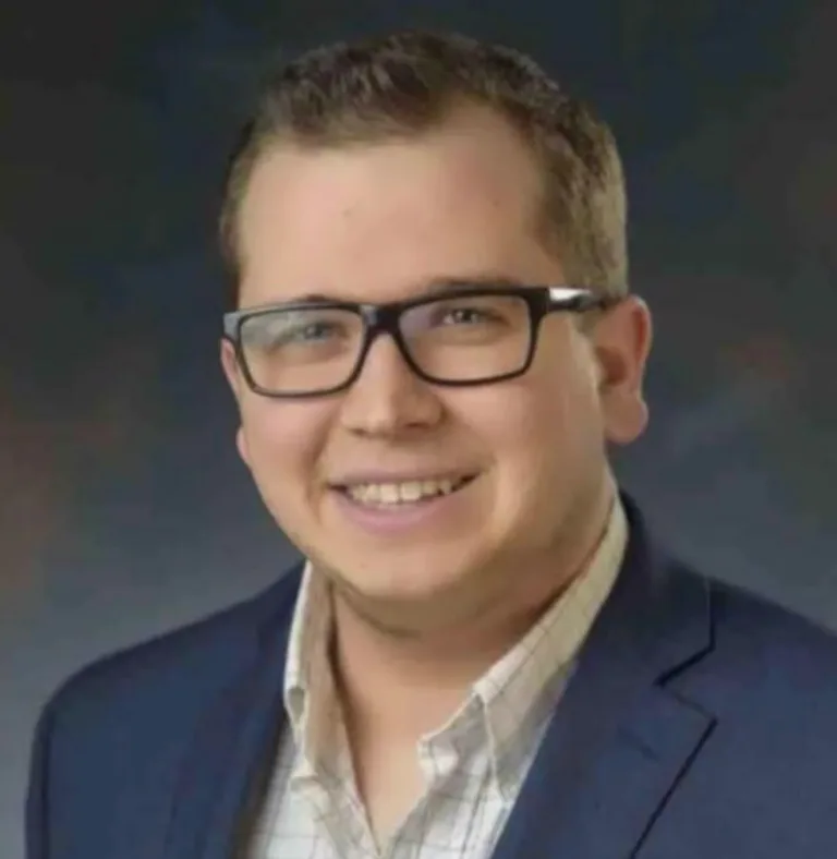 Headshot of a smiling man with glasses and a navy blazer