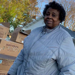 Smiling woman in a light puffer jacket beside cardboard food boxes