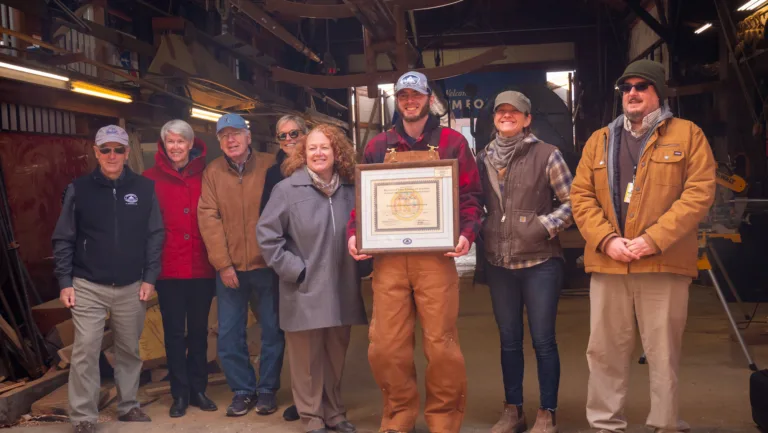 Group holding a framed certificate at an apprenticeship graduation in a workshop