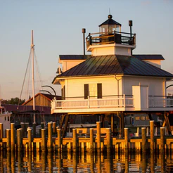White lighthouse on pilings at sunset beside a dock