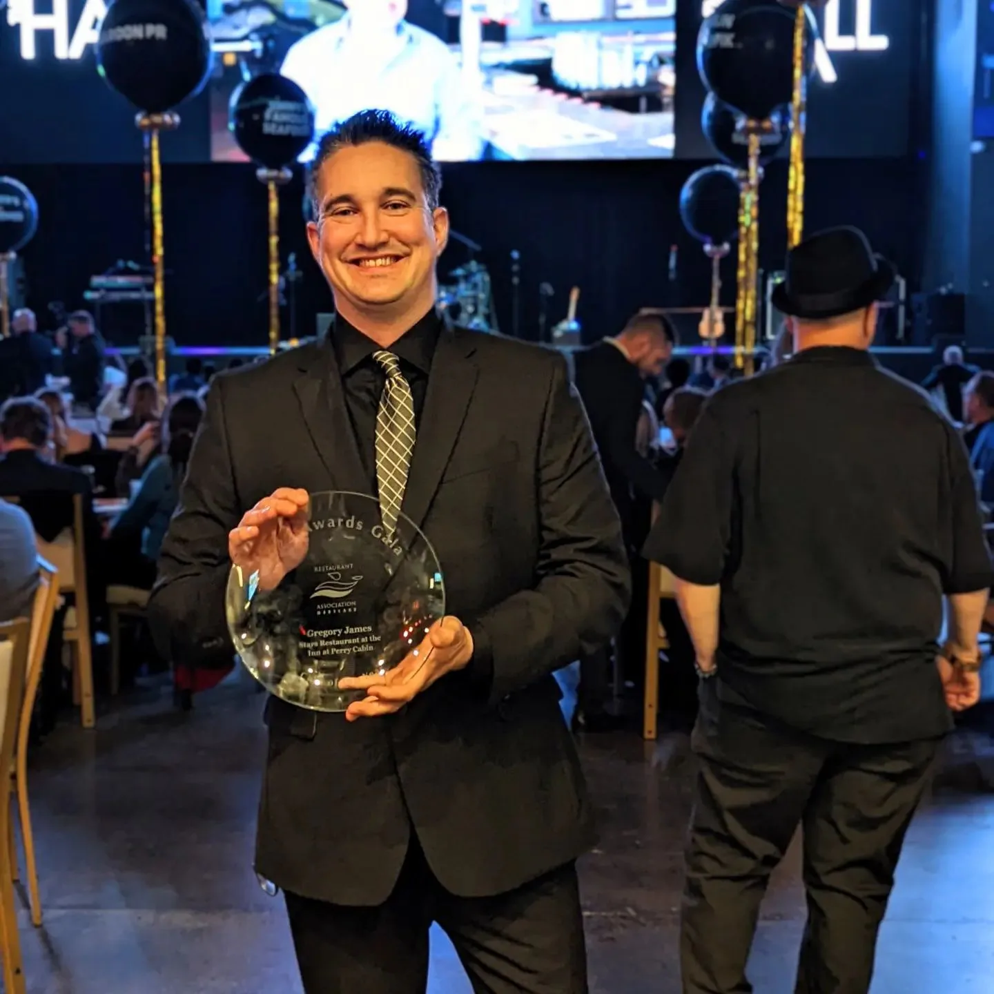 Smiling man in dark suit holding a glass award at an event