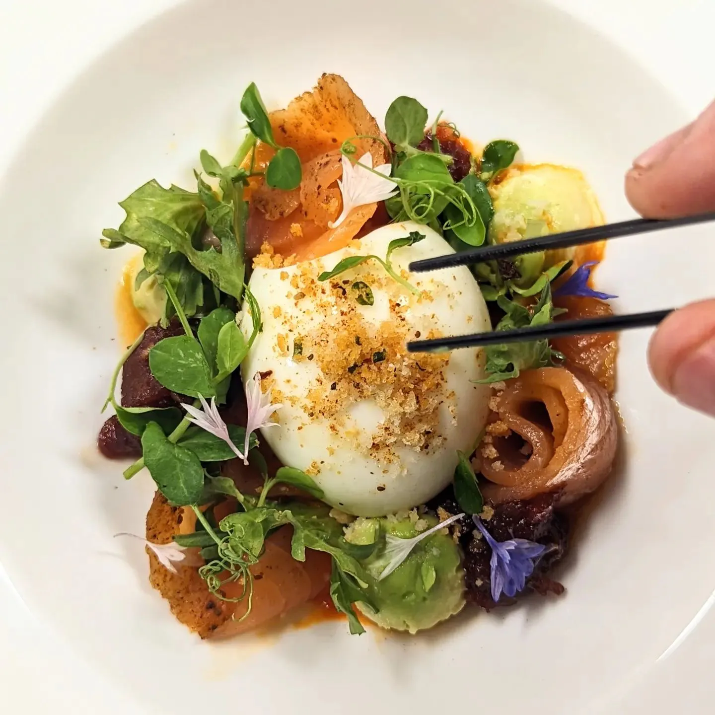 Plated dish with soft egg, greens, and crispy garnish, served with chopsticks