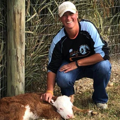 Woman in cap kneeling beside a brown-and-white calf by a wire fence