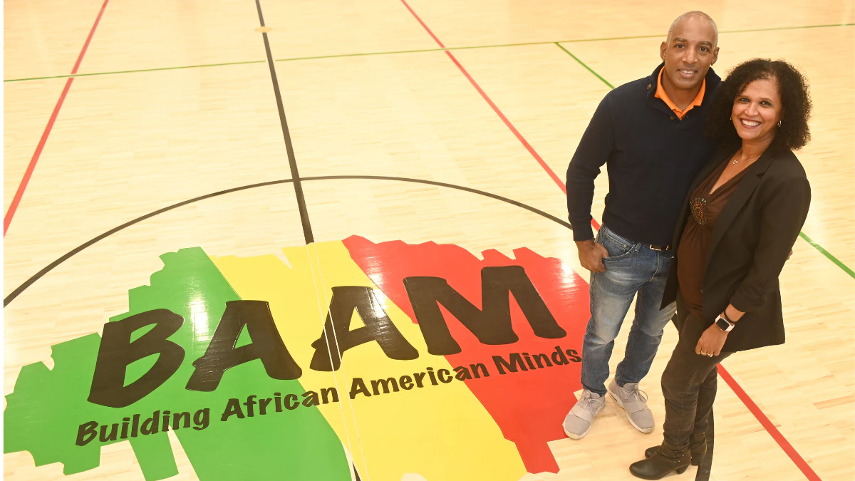 Man and woman on a gym floor beside a BAAM Building African American Minds logo