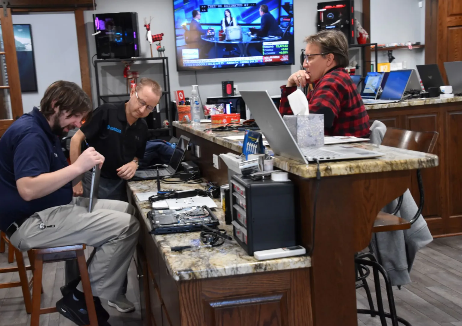 Two men at a computer repair counter helping a customer with a laptop