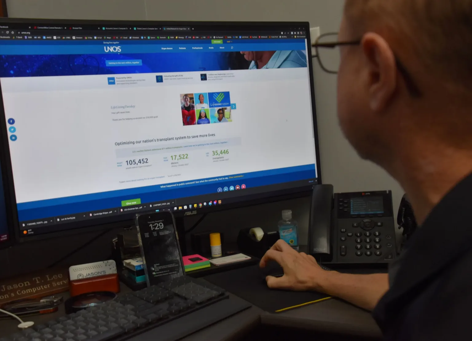Man at a desk reviewing a web page on a monitor beside a phone