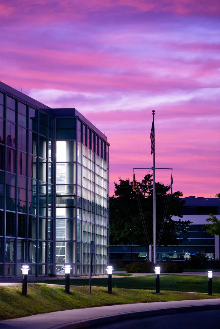 Modern glass office building at dusk under a pink sky with flagpoles