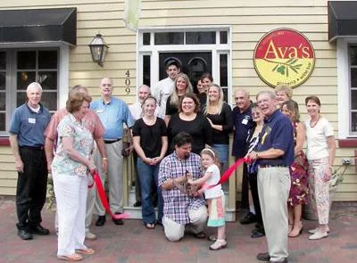 Group posing with red ribbon at a ribbon cutting in front of Ava's restaurant