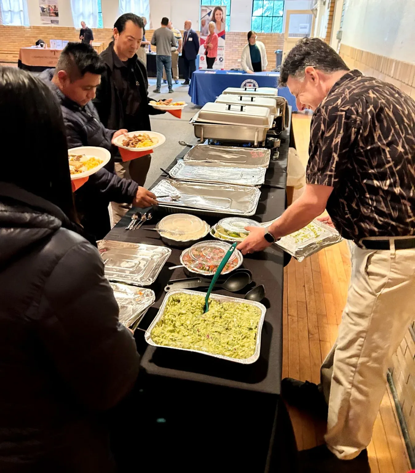 Attendees serving themselves from a buffet of food trays at a community event