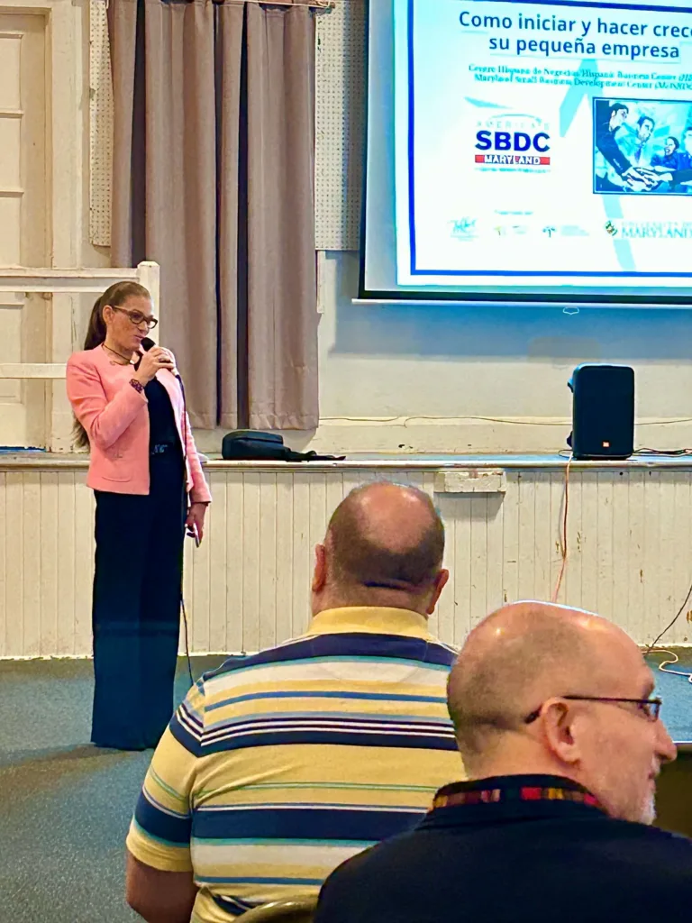 Woman in pink jacket presenting a Spanish-language SBDC slide to an audience