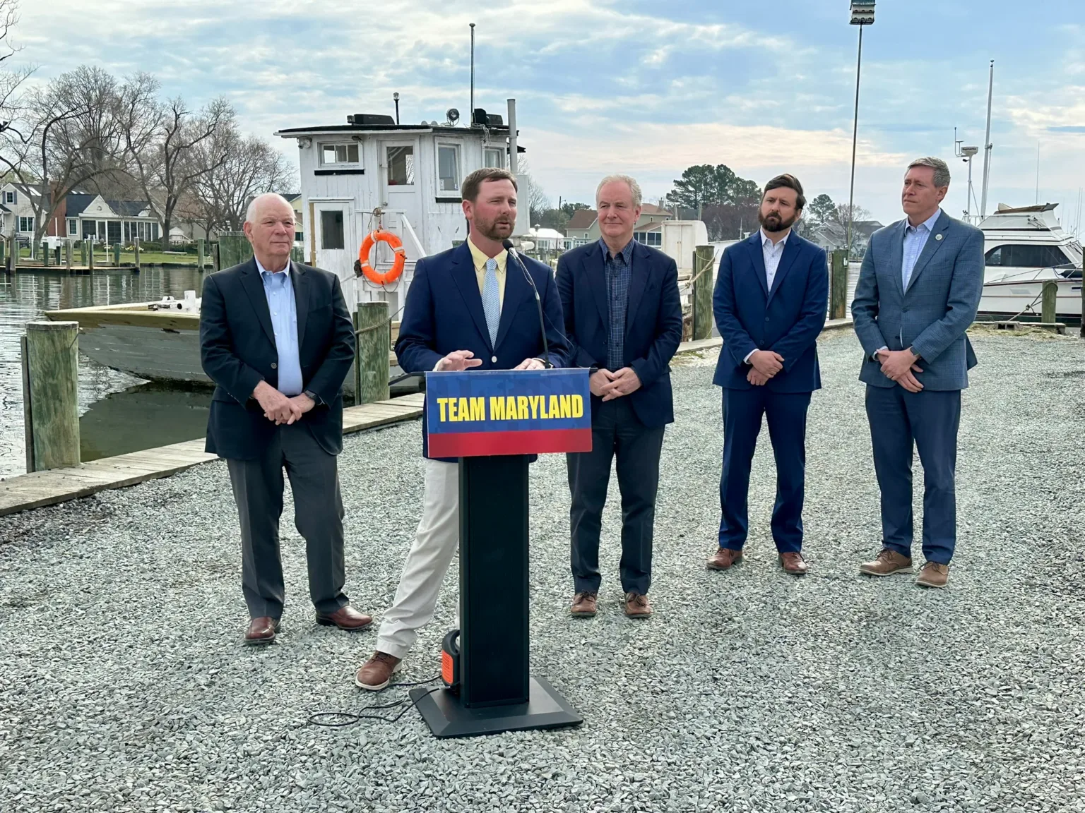 Team Maryland podium with five men in suits on a dock beside a boat
