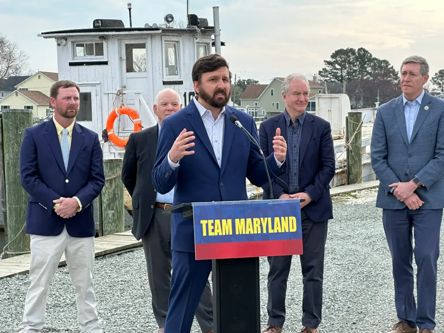 Speaker at Team Maryland podium on a dock with five men standing behind him