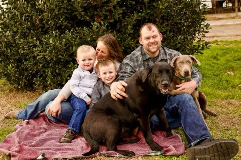 Family of four with two dogs sitting on a blanket outdoors