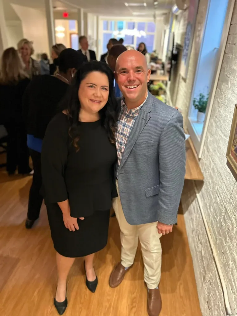 Woman in black dress and man in blue blazer posing in a hallway