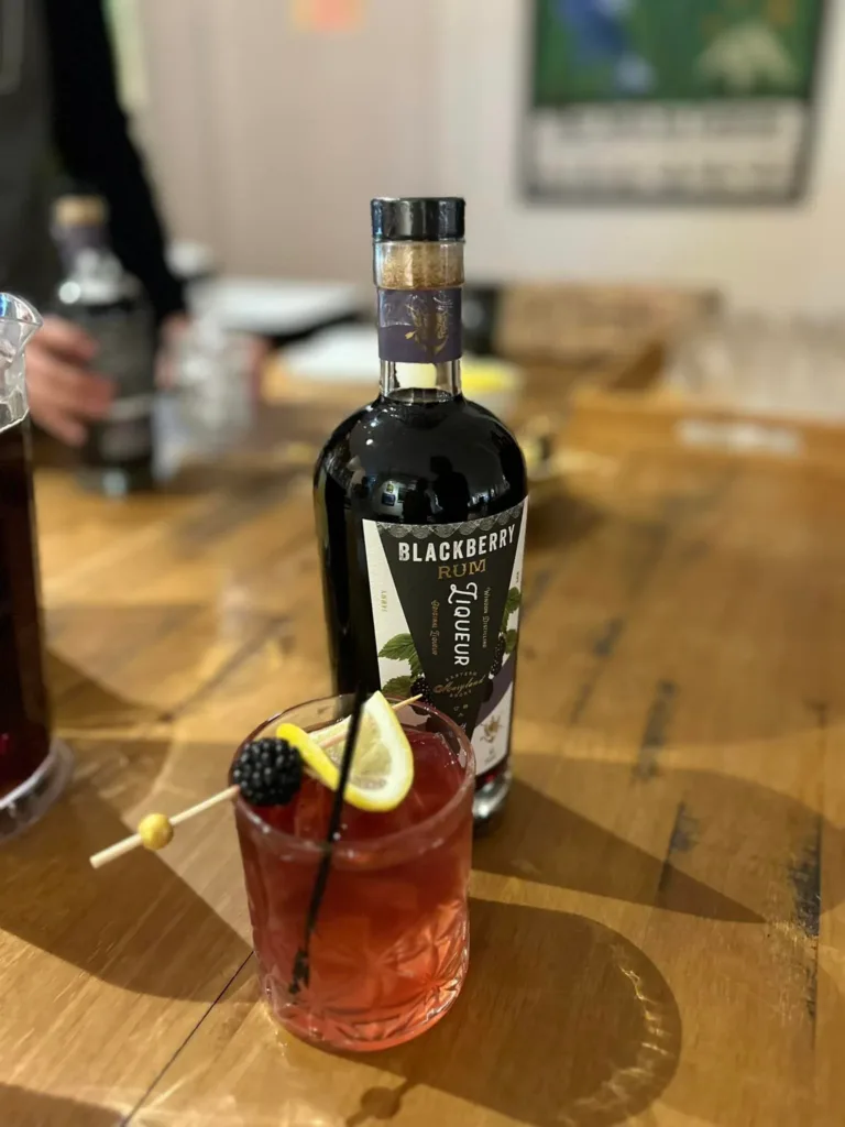 Red cocktail with blackberry garnish beside a bottle labeled Blackberry